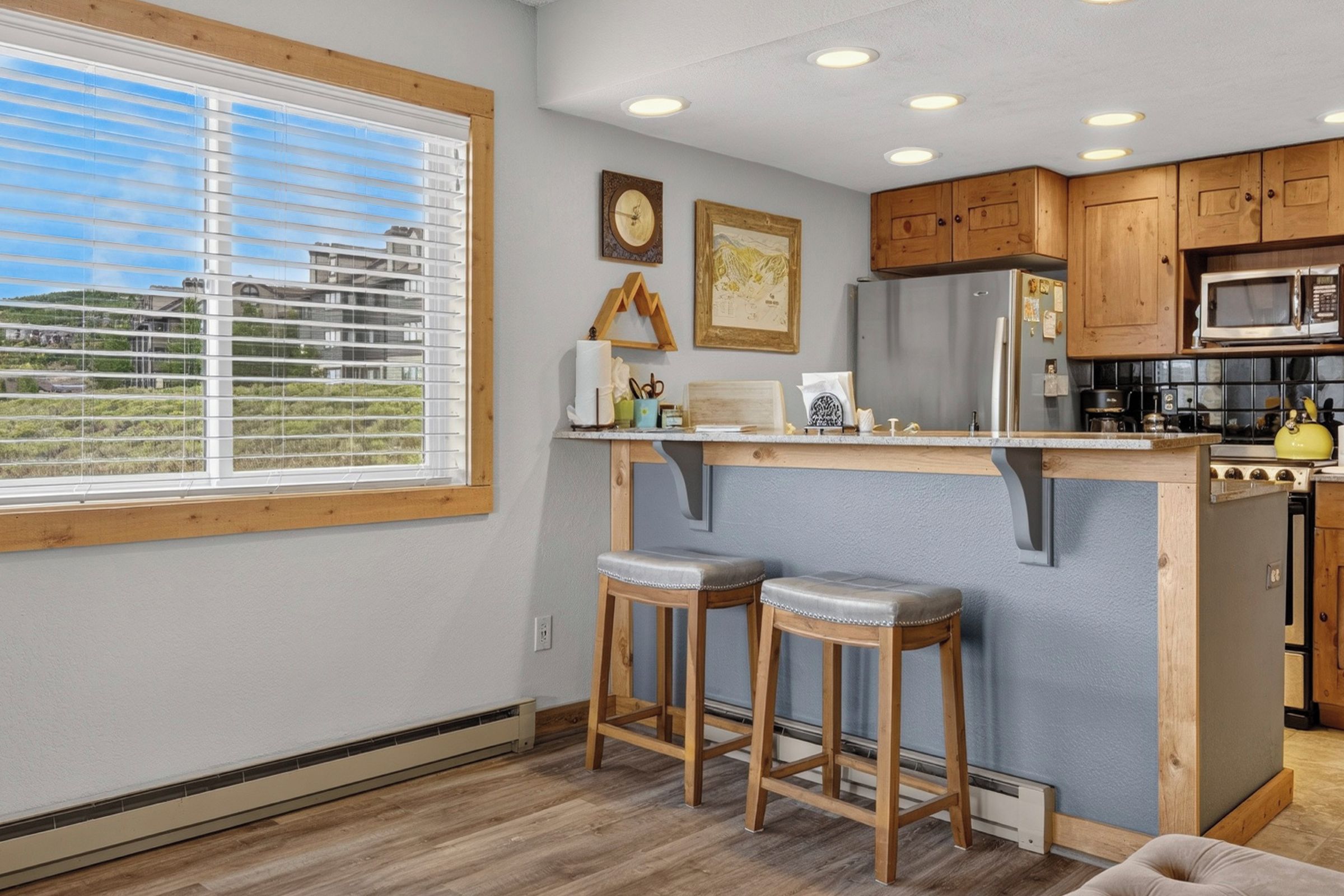 Una cocina con armarios de madera, un refrigerador de acero inoxidable, un microondas y un taburete de bar.