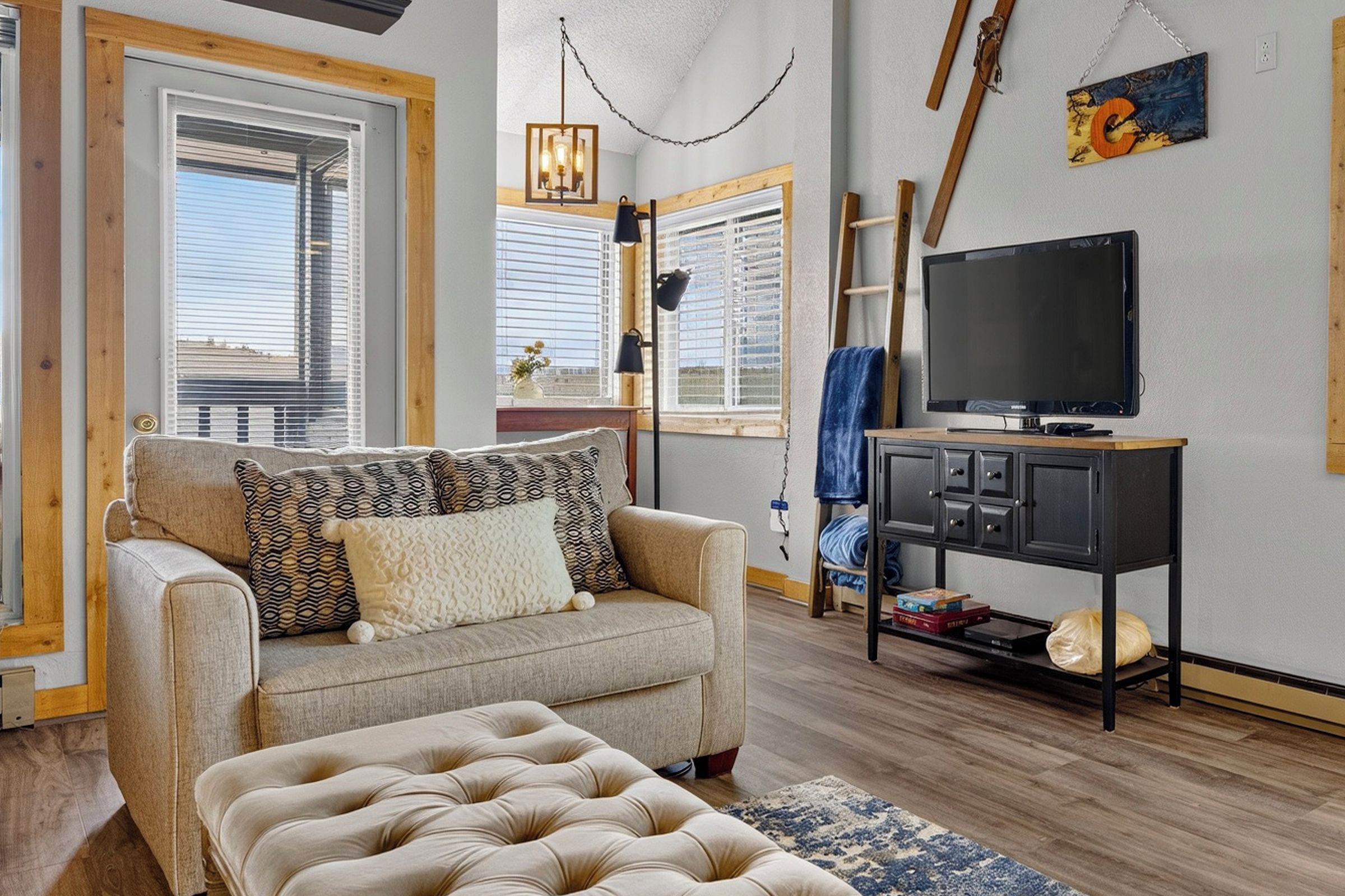 A living room with a sofa, ottoman, TV, and a small table with a TV stand.