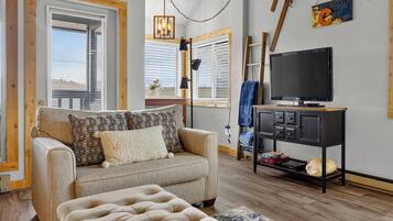 A living room with a sofa, ottoman, TV, and a small table with a TV stand.
