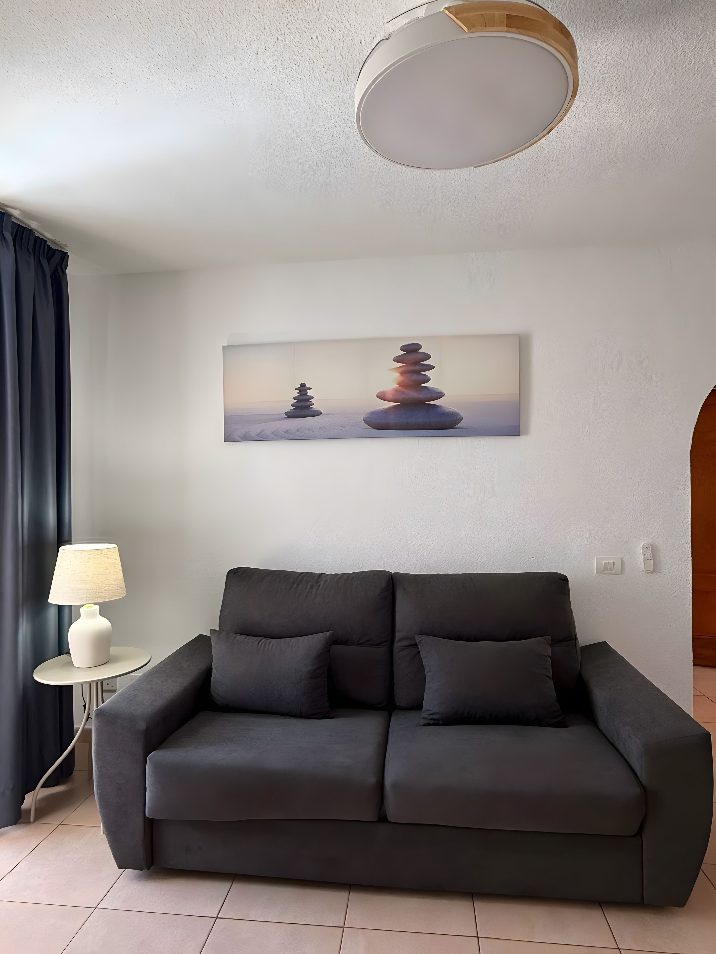 Un salon moderne avec un canapé gris, une lampe et un tableau représentant des pierres empilées.