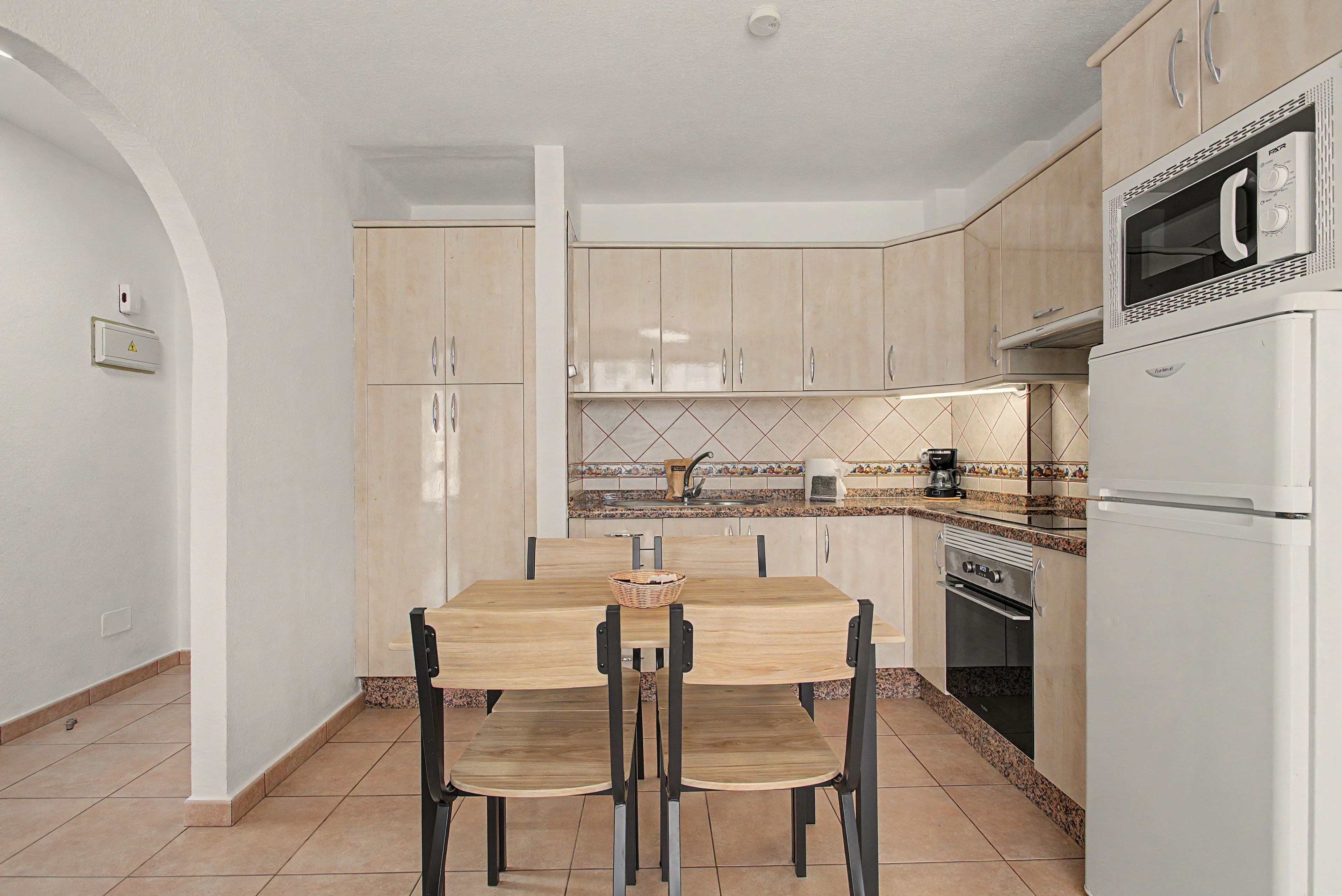 Een moderne keuken met een eettafel, stoelen, een magnetron, een koffiezetapparaat en een fornuis.