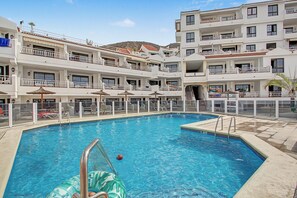 A multi-story hotel with a central swimming pool, balconies with railings, and outdoor seating areas. - Vacation Apartment 'Diamante Sol Los Cristianos' with Shared Pool and Wi-Fi (Los Cristianos)