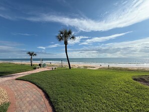 A paved pathway leading to a beach with palm trees and a clear view of the ocean. - Lovely 2-bedroom ocean front penthouse in Ormond Beach (Ormond Beach)