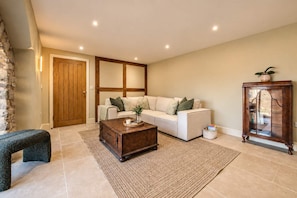 A living room with a sofa, a coffee table, a cabinet, and a stone wall. - Countryside Cottage - 2 En-Suites - Parking for 2 (Talbenny)