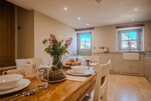 A dining area with a wooden table set for two, a vase with flowers, and a glass of water. - Countryside Cottage - 2 En-Suites - Parking for 2 (Talbenny)