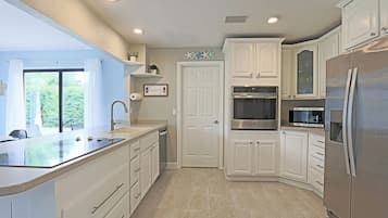 A modern kitchen with white cabinetry, a stainless steel refrigerator, an oven, and a microwave.