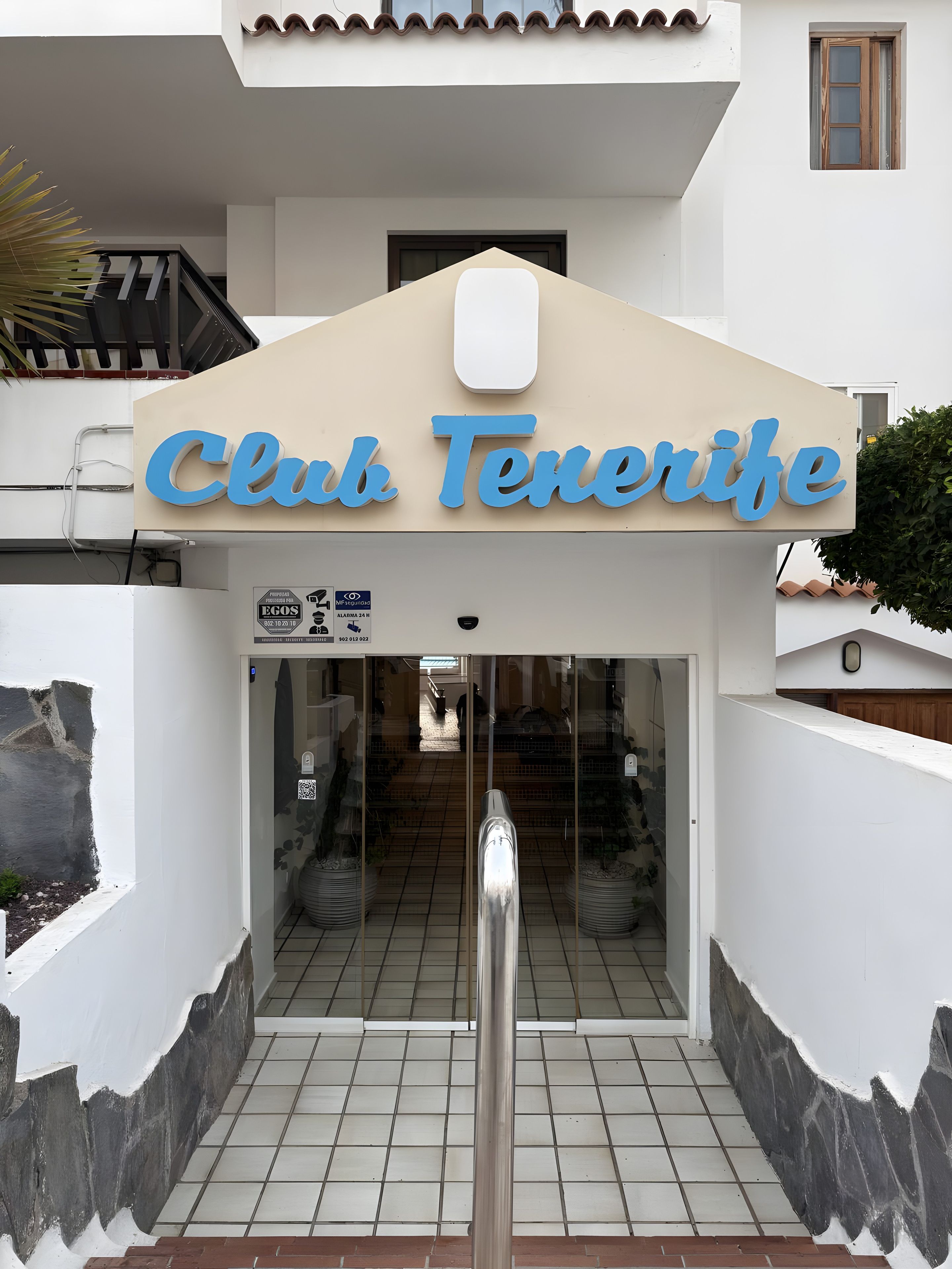 En indgang til Club Tenerife med fliset gulv, en metal trappe og et skilt over døren.