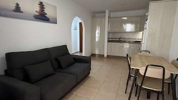 Un salon moderne avec un canapé noir, une table à manger avec des chaises et un coin cuisine équipé de placards et d’un réfrigérateur.