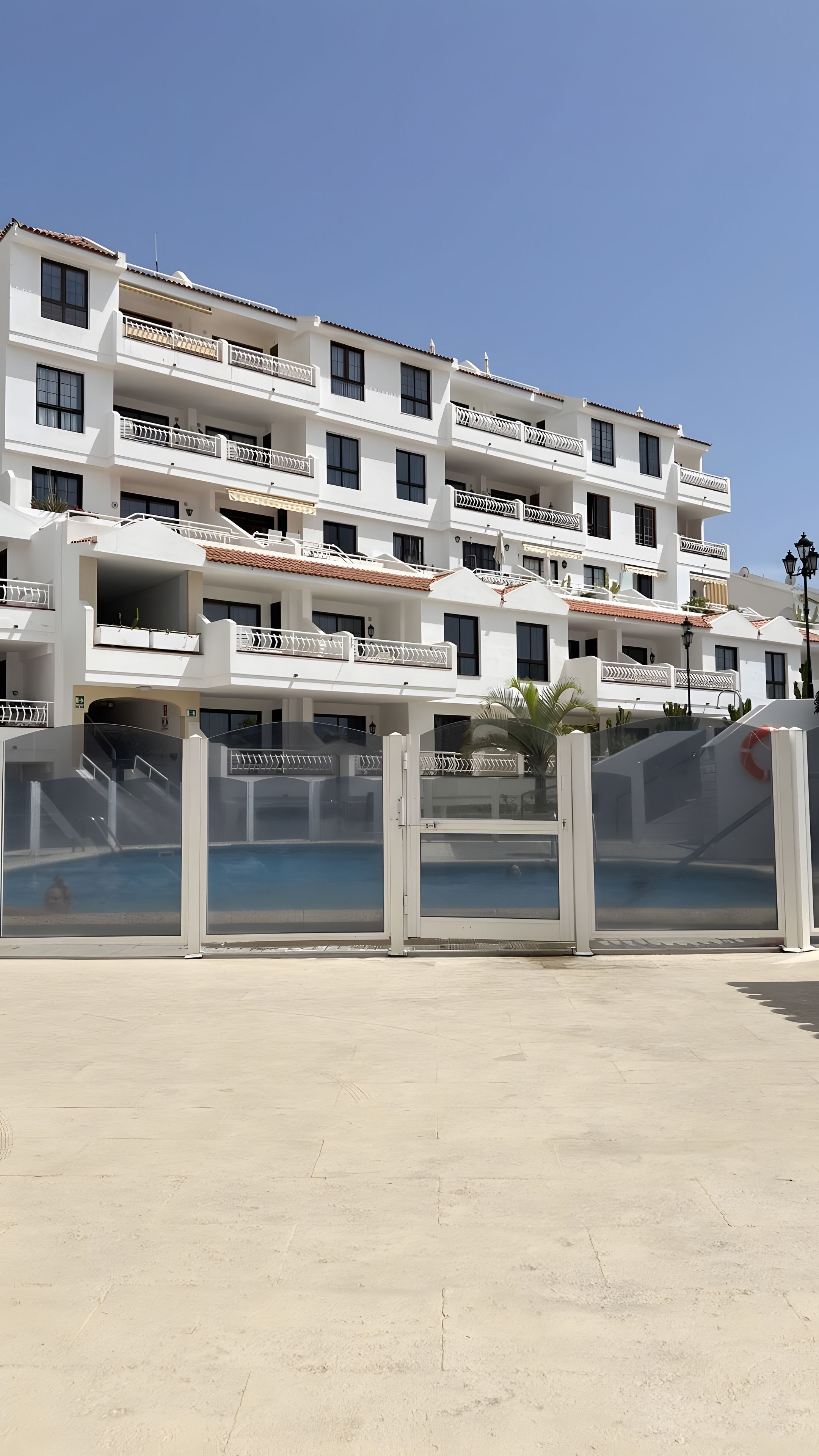 A multi-story hotel with balconies, a swimming pool, and a clear sky.