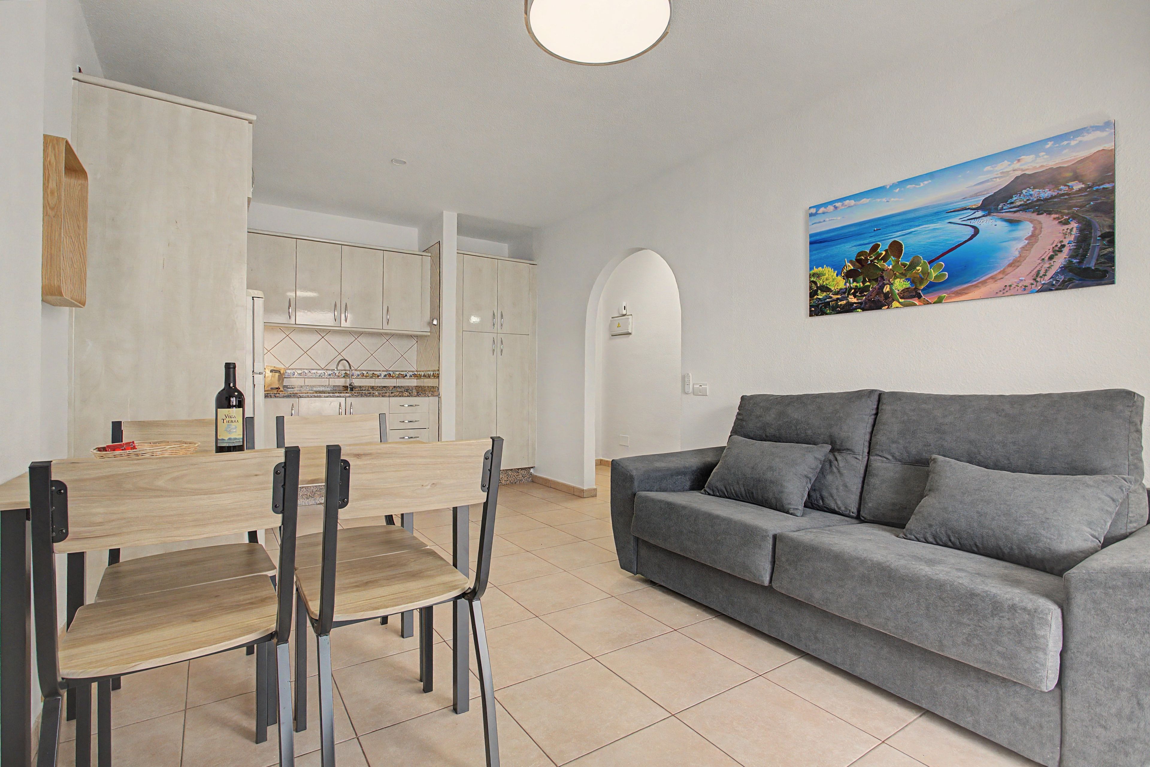 A modern living space with a dining area, a grey sofa, and a kitchen.