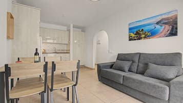 A modern living space with a dining area, a grey sofa, and a kitchen.