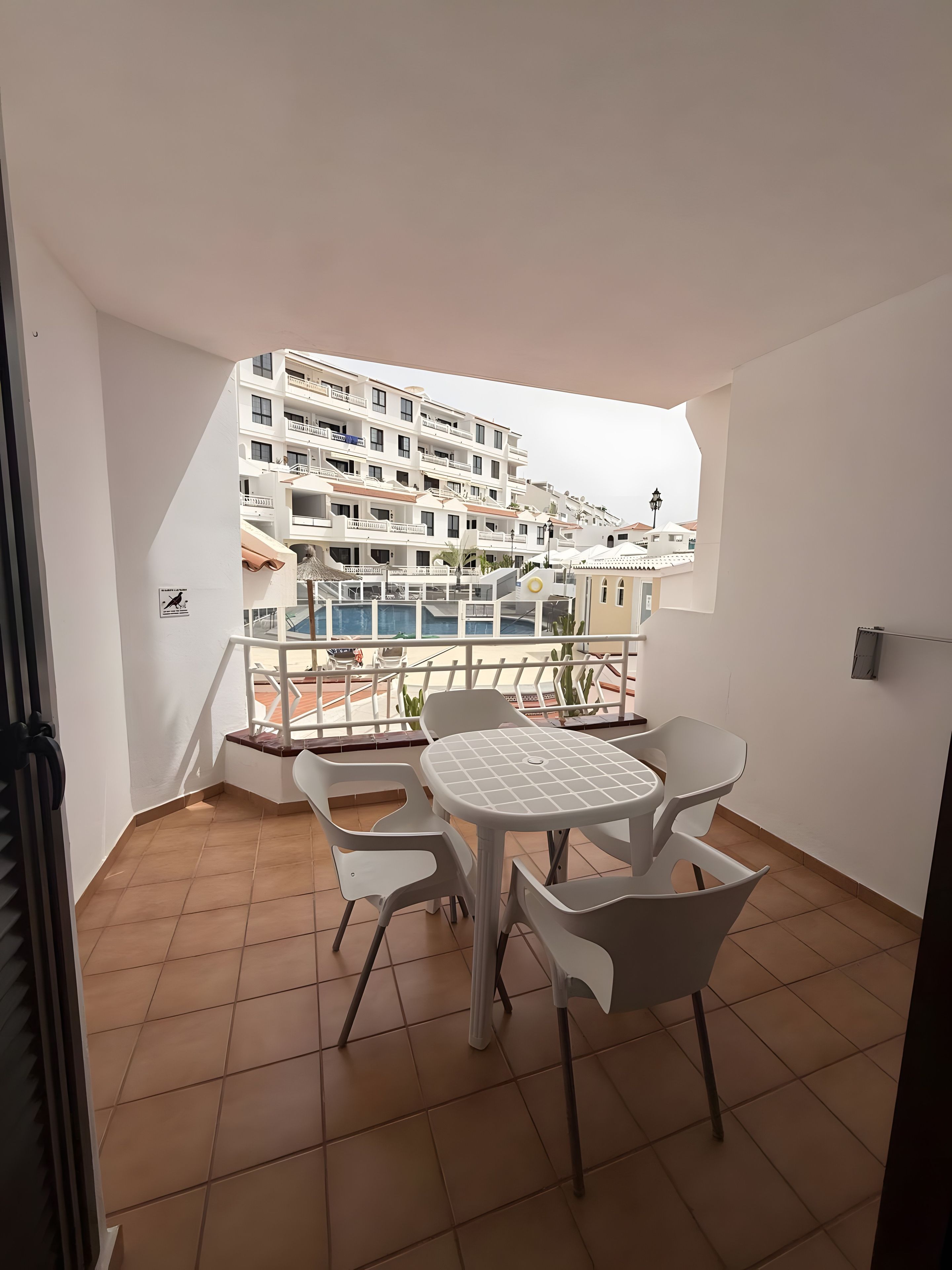 Un balcon avec une table et des chaises, une vue sur un immeuble doté de nombreux balcons et un sol carrelé.