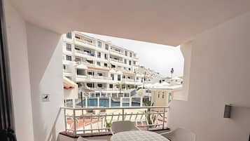 Un balcon avec une table et des chaises, une vue sur un immeuble doté de nombreux balcons et un sol carrelé.
