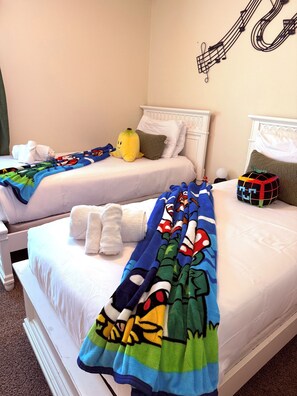 Two beds with white bedding, a yellow banana-shaped pillow, and a blue blanket with cartoon characters. - Family Vacation Home Disney 8 people -Private Pool & Game Room in Kissimmee (Kissimmee)