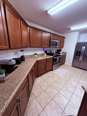 A kitchen with wooden cabinets, a microwave, an oven, a refrigerator, and a granite countertop.