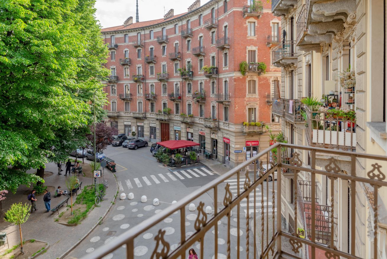 A multi-story building with balconies, a pedestrian crossing, and a street with parked cars.