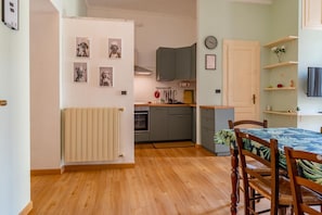 A compact kitchen with grey cabinets, a wooden floor, and a dining area with a table and chairs. - In the vibrant heart of Turin, this flat is all about atmosphere: a spacious, light-filled living room with a fully equipped kitchen, two double bedrooms, a sofa bed and two balconies (one overlooking Largo Montebello, the other a more intimate internal  (Torino)