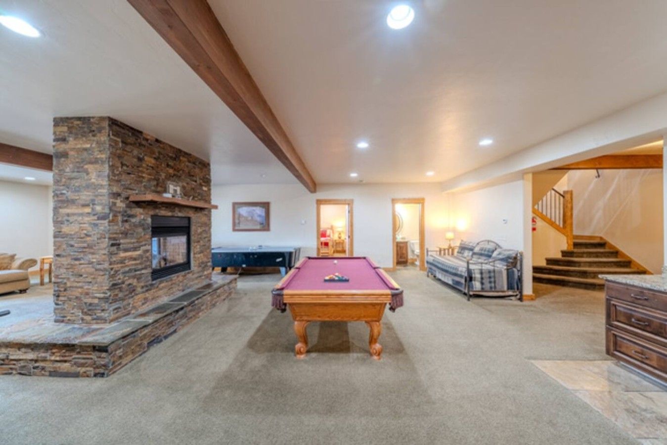 A spacious living area with a pool table, a fireplace, and a staircase leading to another level.