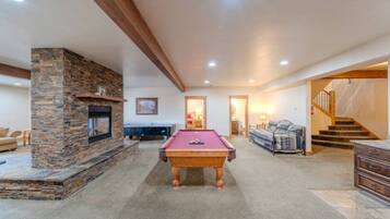 A spacious living area with a pool table, a fireplace, and a staircase leading to another level.