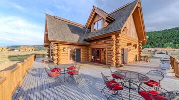 A log cabin with a deck, outdoor seating, and a view of the surrounding landscape.