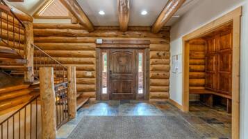 A log cabin interior with a wooden staircase, a central door, and a stone-tiled floor.
