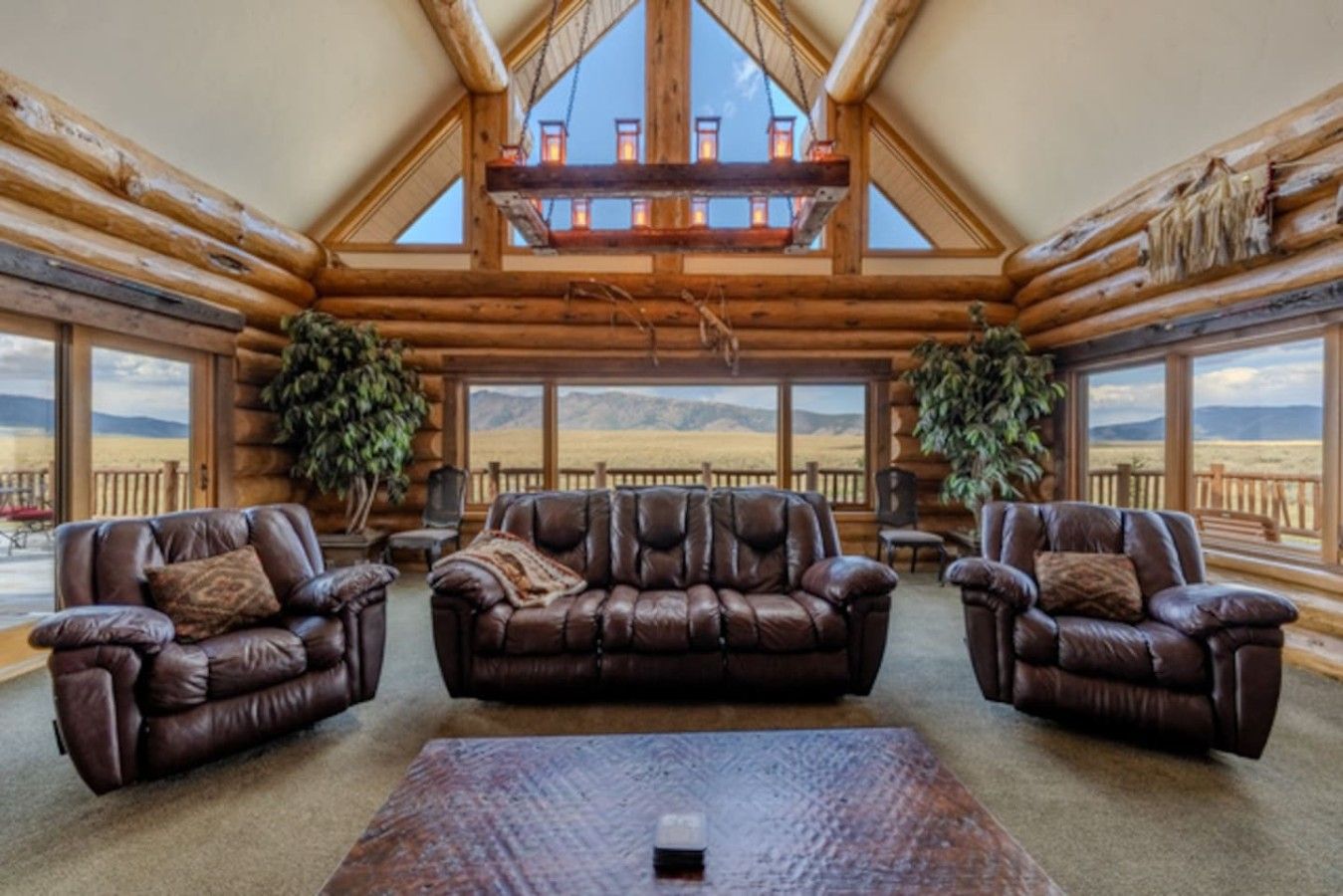 A log cabin interior with a high ceiling, leather sofas, and large windows offering a view of the outdoors.
