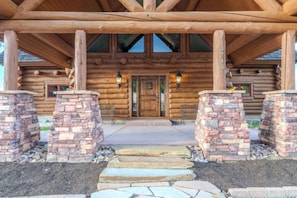 A log cabin with a stone entrance, wooden beams, and two lantern-style lights. - Yellowstone Pointe Lodge - Sleeps 30, 20minToYellowstone, Movie Room, Games! (Island Park)