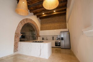 A kitchen with a central island, a brick wall, and a hanging light fixture. - 11 Bedroom Villa in the Old City (Cartagena de Indias)