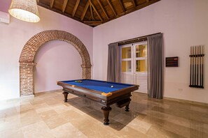 Una mesa de billar en una habitación con un arco de ladrillo, una puerta con cortinas y un techo con vigas de madera.