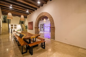 A dining area with a long wooden table and benches, a staircase with a railing, and a brick archway leading to another room. - 11 Bedroom Villa in the Old City (Cartagena de Indias)