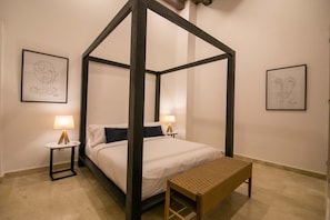 A four-poster bed with white bedding and dark pillows, flanked by two bedside tables with lamps, in a room with plain walls and a tiled floor. - 11 Bedroom Villa in the Old City (Cartagena de Indias)