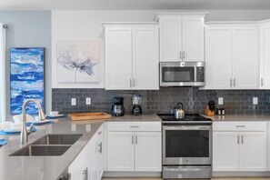 Una cucina moderna con mobili bianchi, elettrodomestici in acciaio inossidabile e una parete rivestita di piastrelle.