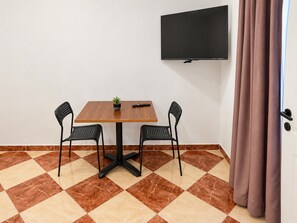 A room with a wooden table, two chairs, a potted plant, a flat-screen TV, and a door with a curtain. - Vienna on Your Doorstep 1BR (Wien)