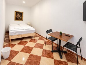 A bedroom with a bed, a wooden table, two chairs, a small potted plant, and a painting on the wall. - Vienna on Your Doorstep 1BR (Wien)