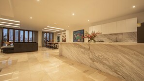 A modern kitchen with marble countertops, a dining area with a bench, and a view of the city through large windows. - Modern 7 Bedroom Mansion in Old City (Cartagena de Indias)