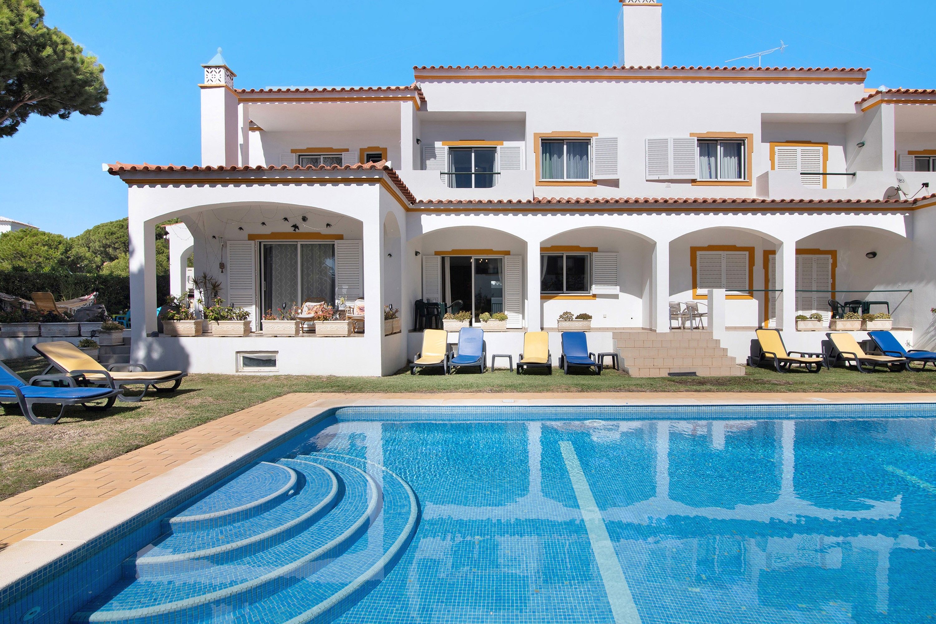 A two-story villa with a swimming pool, outdoor seating, and a garden.