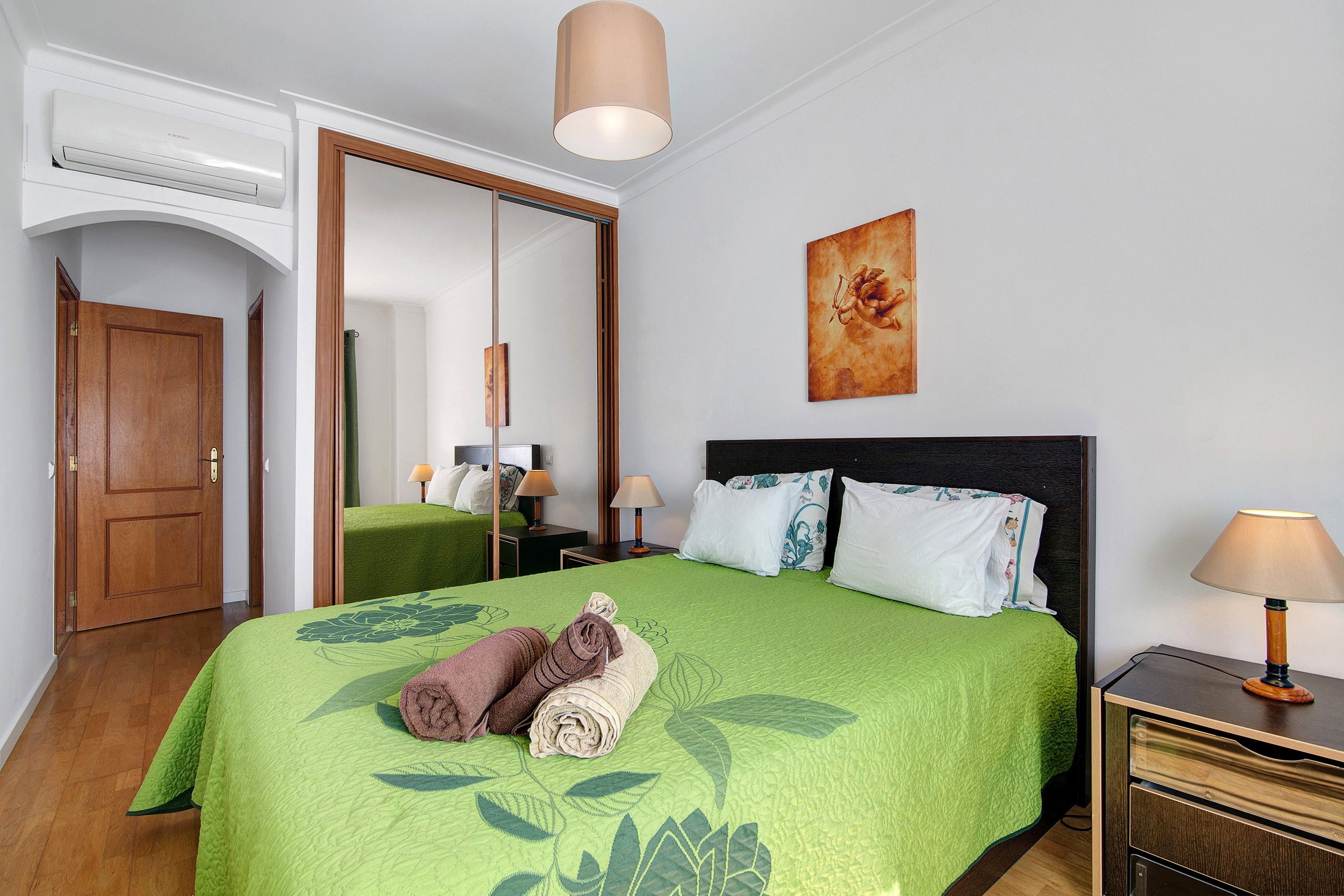 A hotel room with a bed, a mirror, a painting, and a nightstand.