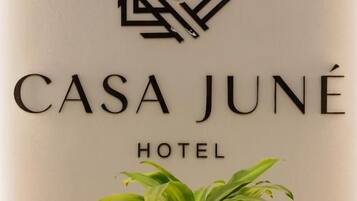 Een bordje voor CASA JUNÉ HOTEL, met een logo boven de naam en een bloempot eronder.
