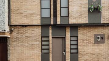 A building facade with a brick exterior, a central door, and a window with a plant.