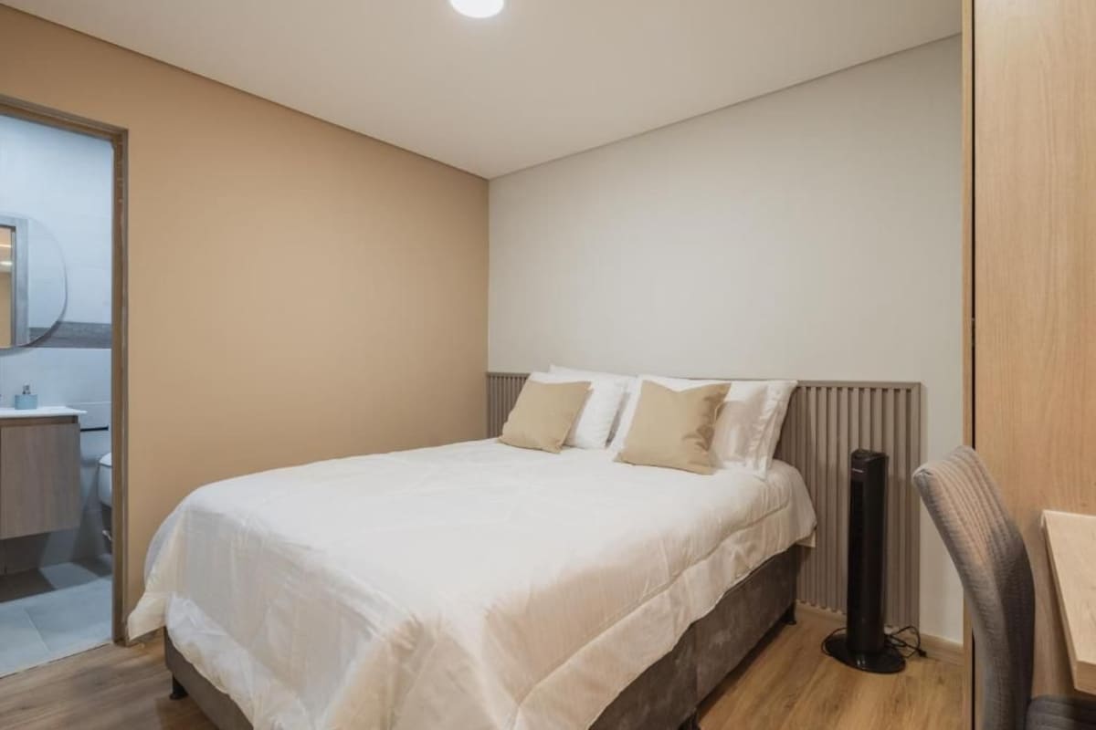 A bedroom with a bed, bedside table, chair, and a radiator.