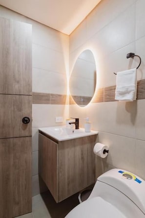 A bathroom with a wooden vanity, a mirror with lighting, a toilet, and a towel rack. - Casa Juné (Pereira)