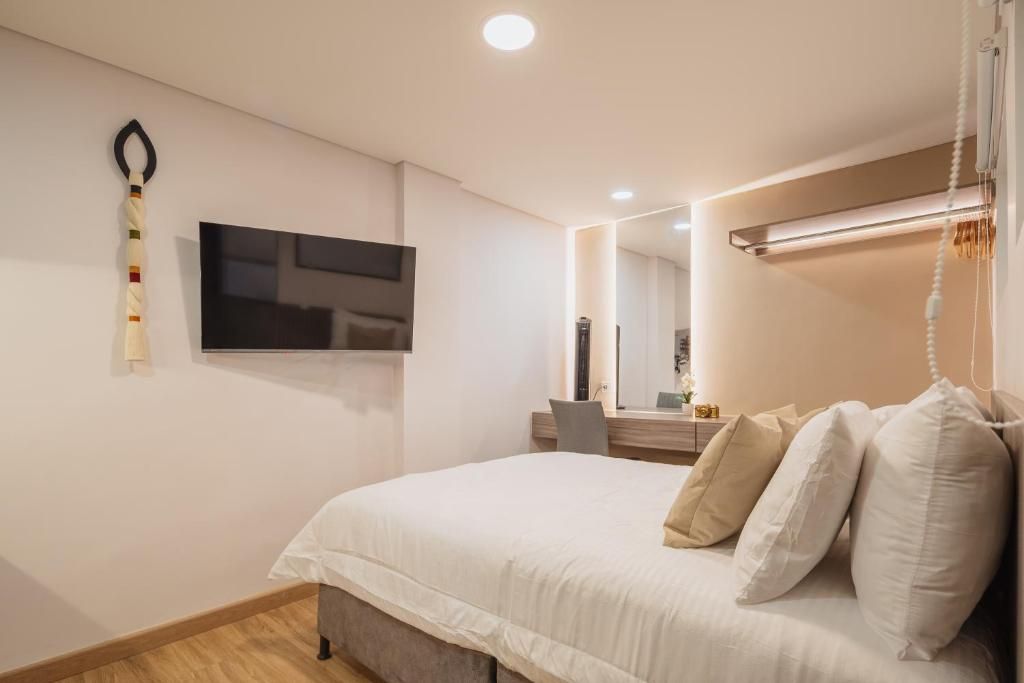 A modern bedroom with a bed, a flat-screen TV mounted on the wall, a bedside table, and a mirror.