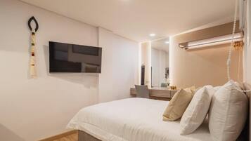 A modern bedroom with a bed, a flat-screen TV mounted on the wall, a bedside table, and a mirror.