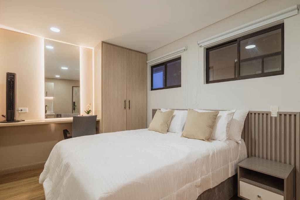 Un dormitorio moderno con una cama grande, mesitas de noche, un escritorio y un espejo.