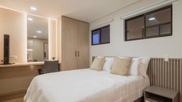 Un dormitorio moderno con una cama grande, mesitas de noche, un escritorio y un espejo.