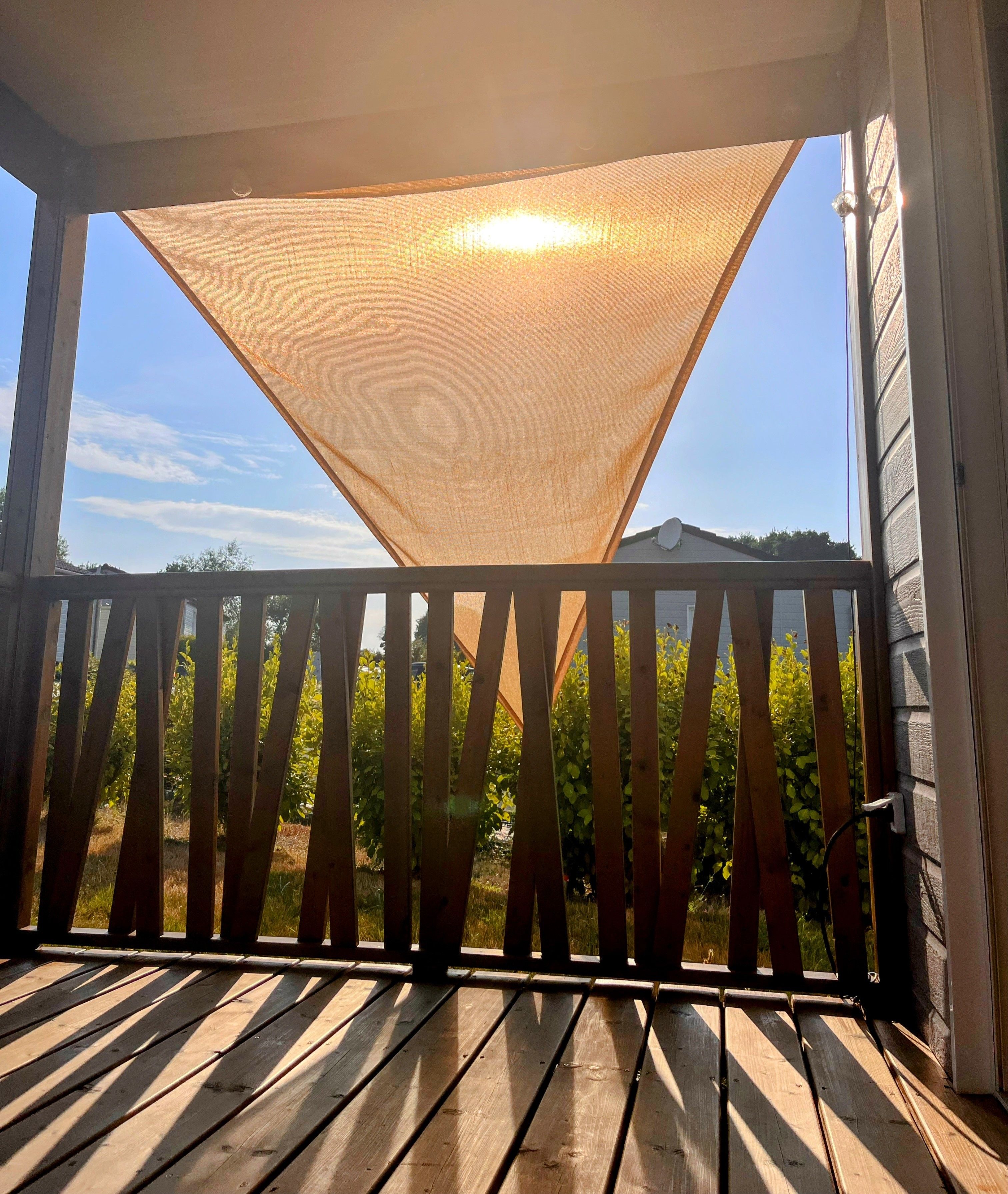 Une terrasse en bois dotée d’un auvent en treillis, de rampes en bois et offrant une vue sur la verdure et une maison en arrière-plan.