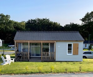 Ein kleines, eingeschossiges Haus mit einem Ziegeldach, einer Veranda mit Stühlen und einem Rasen.