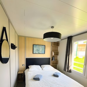 Une chambre d’hôtel avec un lit, une table de chevet, une lampe fixée au mur, un tableau et une fenêtre avec des rideaux.