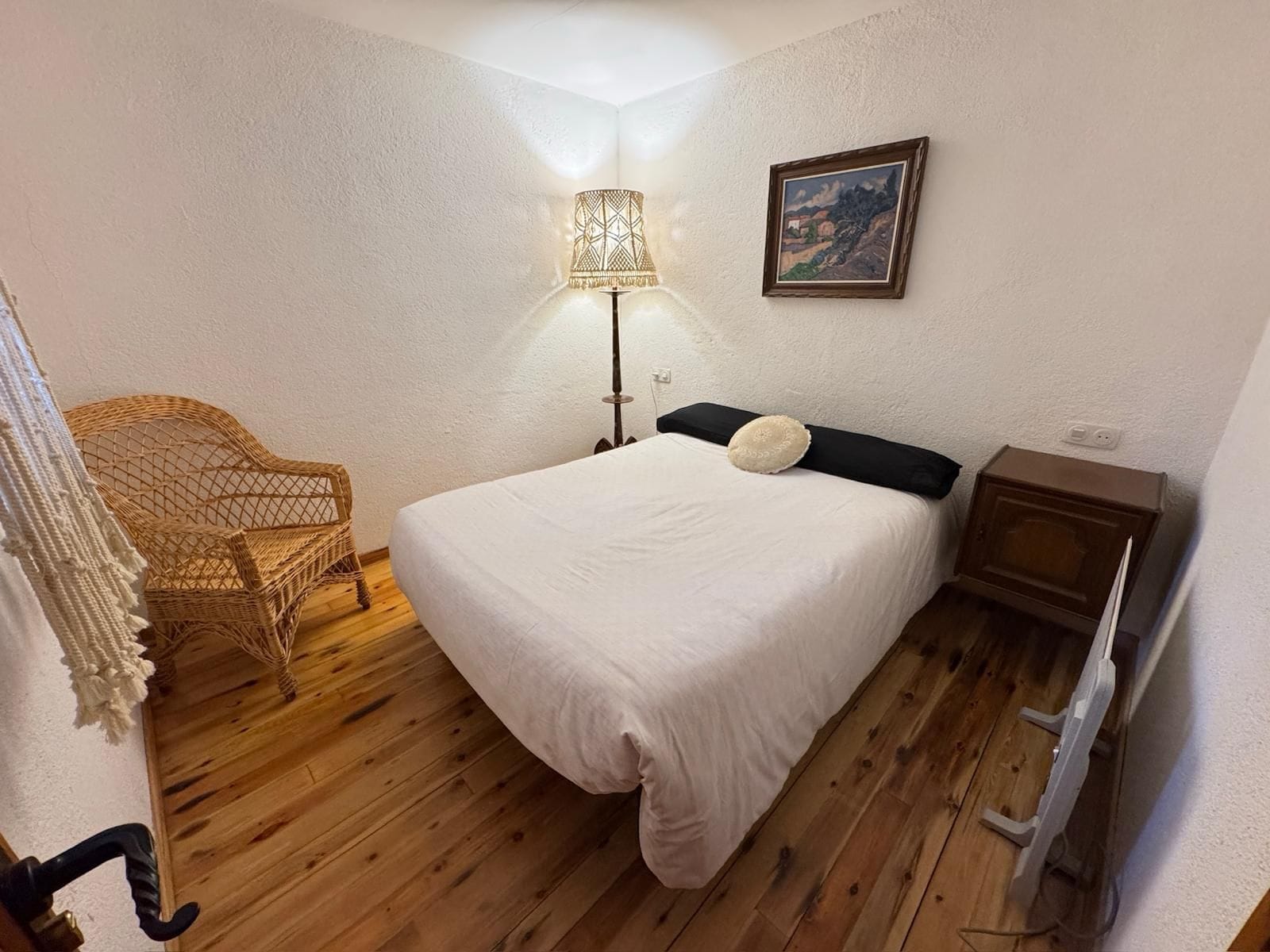 Un dormitorio con cama, lámpara, silla y un cuadro en la pared.