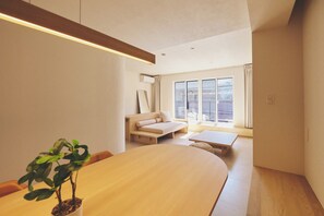 A modern living room with a wooden dining table, a sofa, and a large window providing natural light. - New Listing (新宿区中落合１丁目２１－３　中落合ホテル)